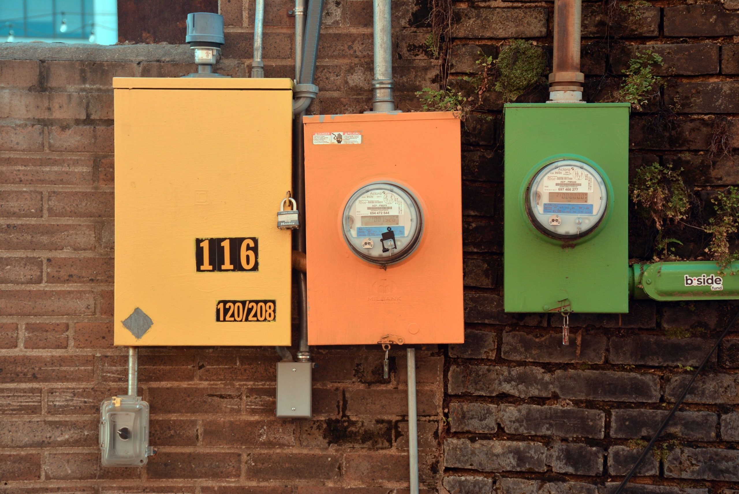 Trois compteurs électriques colorés sur un mur en brique