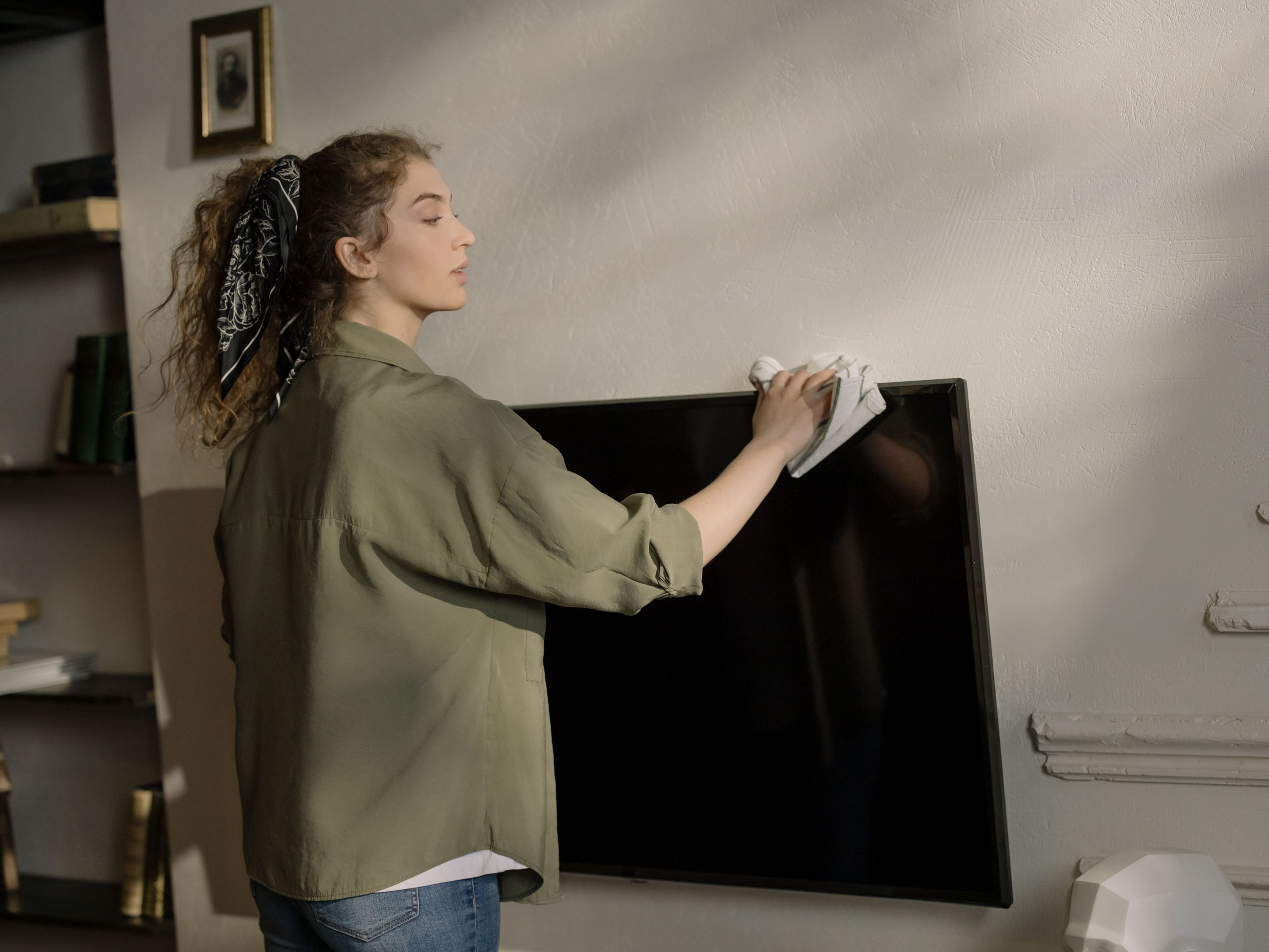 Femme nettoyant l'écran d'une télévision chez elle